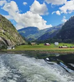 Udsigt fra fjordcruise mod en grøn dal med røde og hvide gårde ved vandet og stejle fjelde
