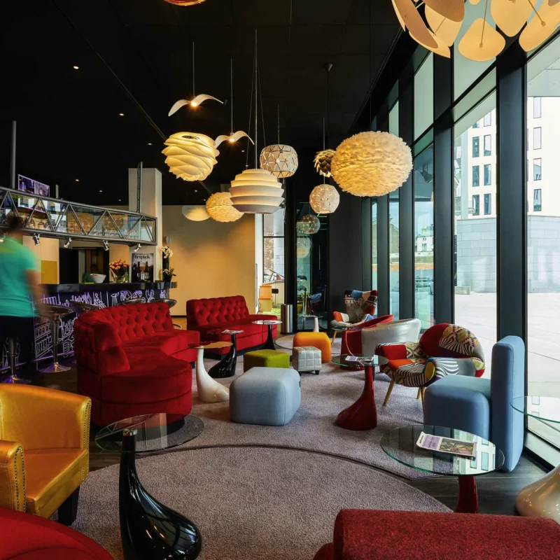 Den farverige lobby og bar på ibis Styles Liège Guillemins med røde lænestole og store lamper