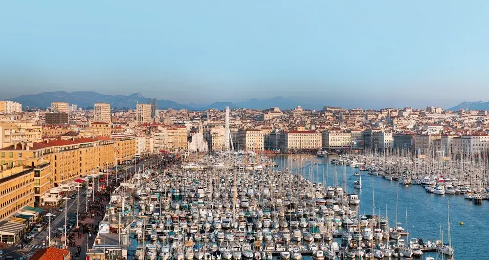 Den gamle havn i Marseille fyldt med sejlbåde, omgivet af lyse bygninger og bakker i baggrunden