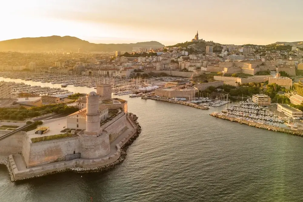 Luftfoto af den gamle havn i Marseille i morgenlys med Notre-Dame de la Garde på bakken over byen
