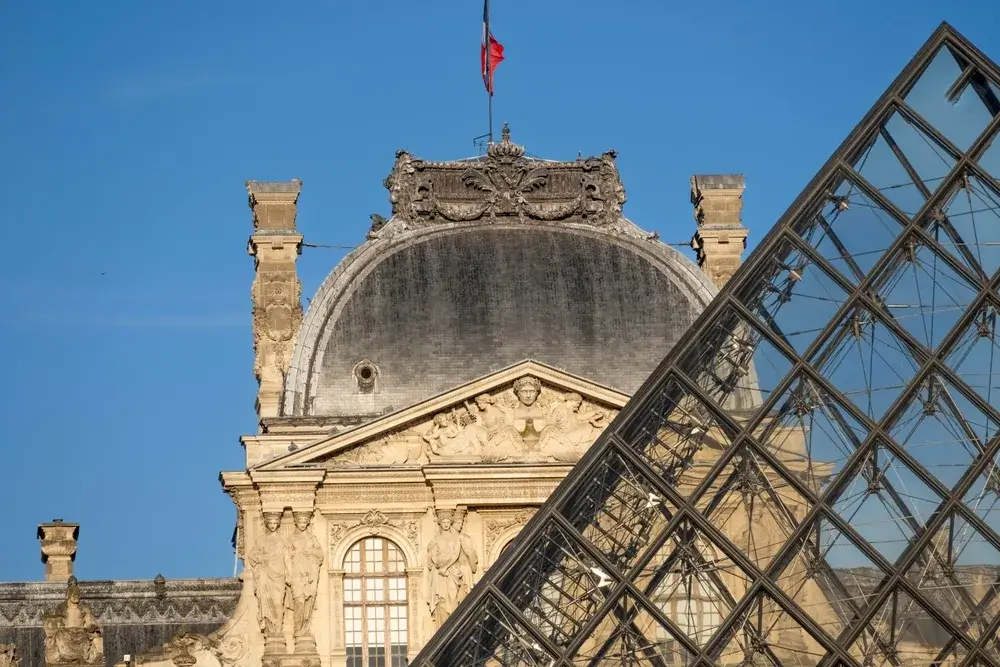 Glaspyramiden foran en af Louvre-paladsets udsmykkede facader under blå himmel i Paris