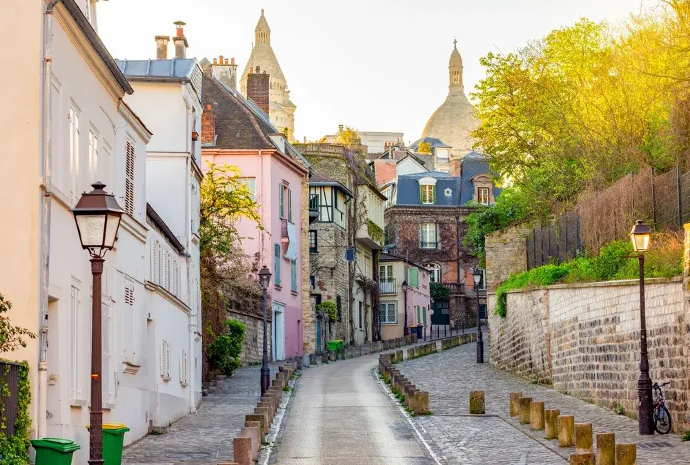 Brostensgade med gadelygter og pastelfarvede huse i Montmartre med Sacré-Cœurs kupler i baggrunden