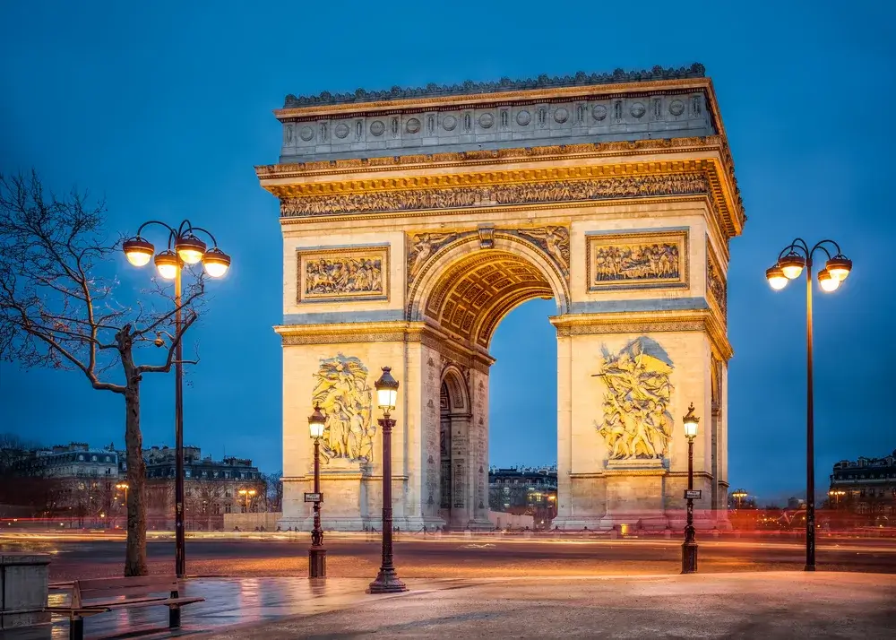 Triumfbuen i Paris oplyst i skumringen med tændte gadelygter foran