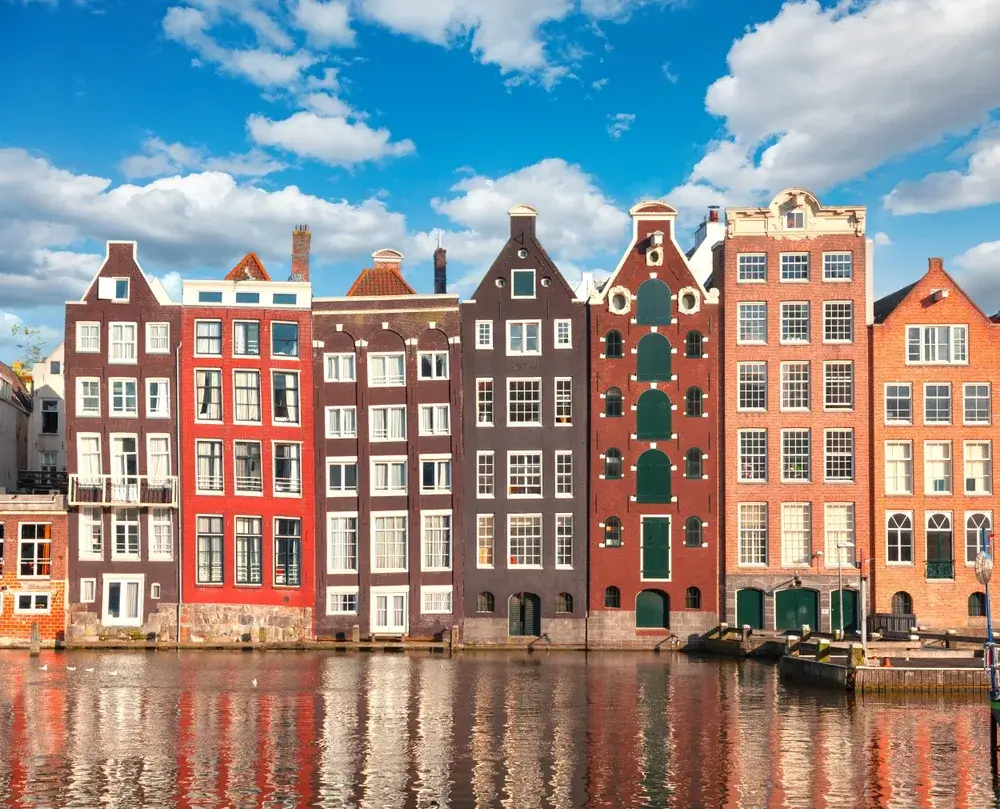 Skæve, smalle gavlhuse ved Damrak i Amsterdam spejler sig i vandet