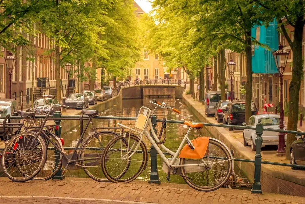 Cykler parkeret ved gelænderet over en trækantet kanal i Amsterdam