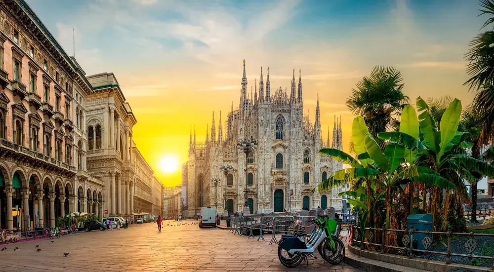 Milanos gotiske domkirke på Piazza del Duomo i gyldent morgenlys med palmer og gamle bygninger på siderne