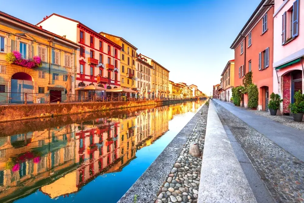 Farverige huse langs kanalen Naviglio Grande i Milano, spejlet i vandet i morgenlys
