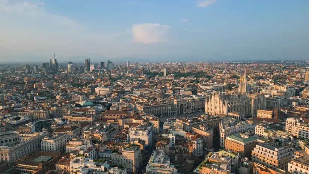 Udsigt over Milanos tage med domkirken i midten og moderne skyskrabere i horisonten under klar himmel