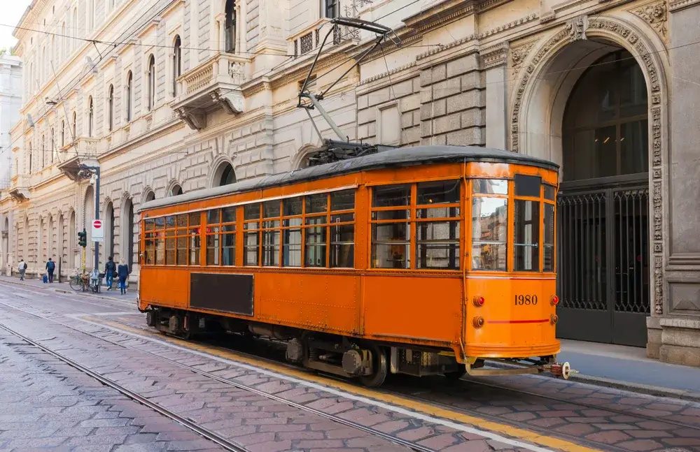 Orange historisk sporvogn kører gennem en brostensgade i Milanos centrum foran lyse bygninger