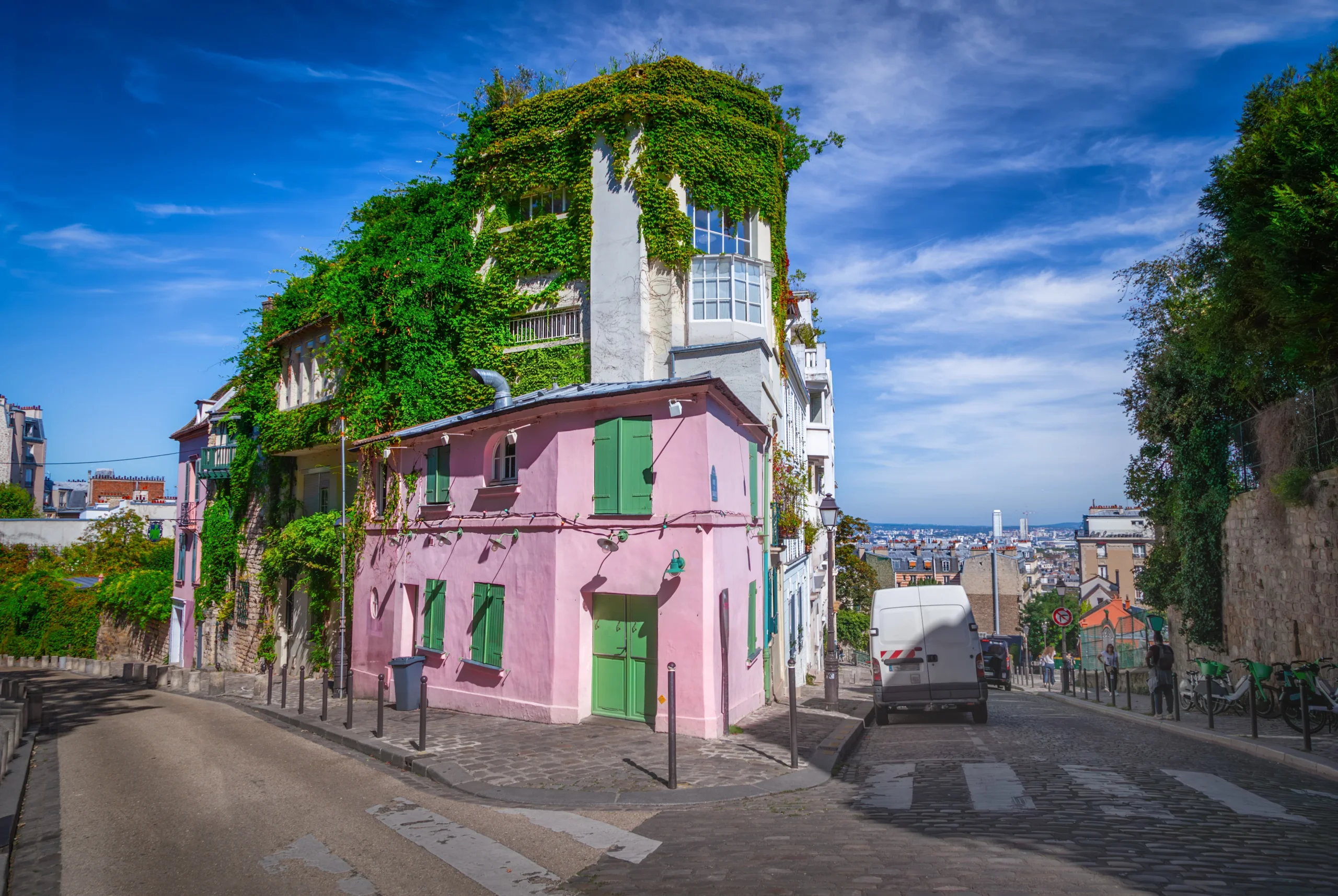 Lyserødt hus på et gadehjørne i Montmartre med grønne træer