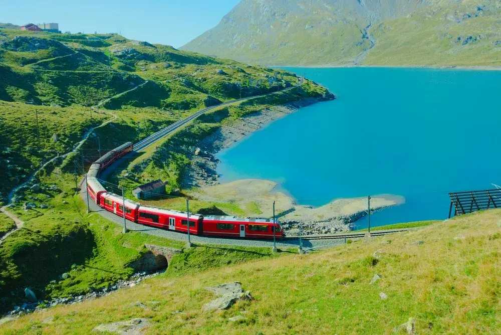 Rødt Bernina Express-tog kører langs Lago Bianco på Bernina-passet med bjerge i baggrunden