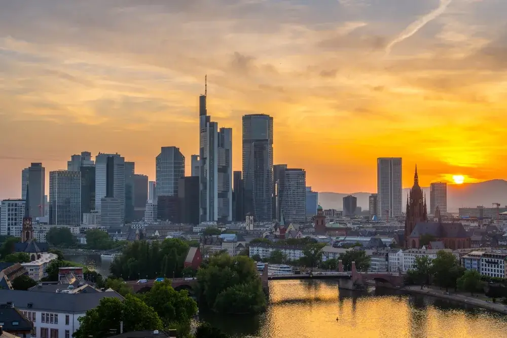 Frankfurts skyskrabere og floden Main i orange solnedgangslys med domkirkens tårn til højre