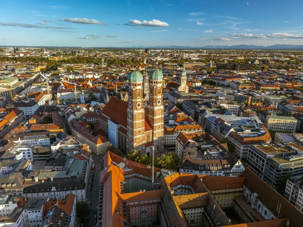 Frauenkirches to tårne med løgkupler over Münchens røde tegltage set fra luften