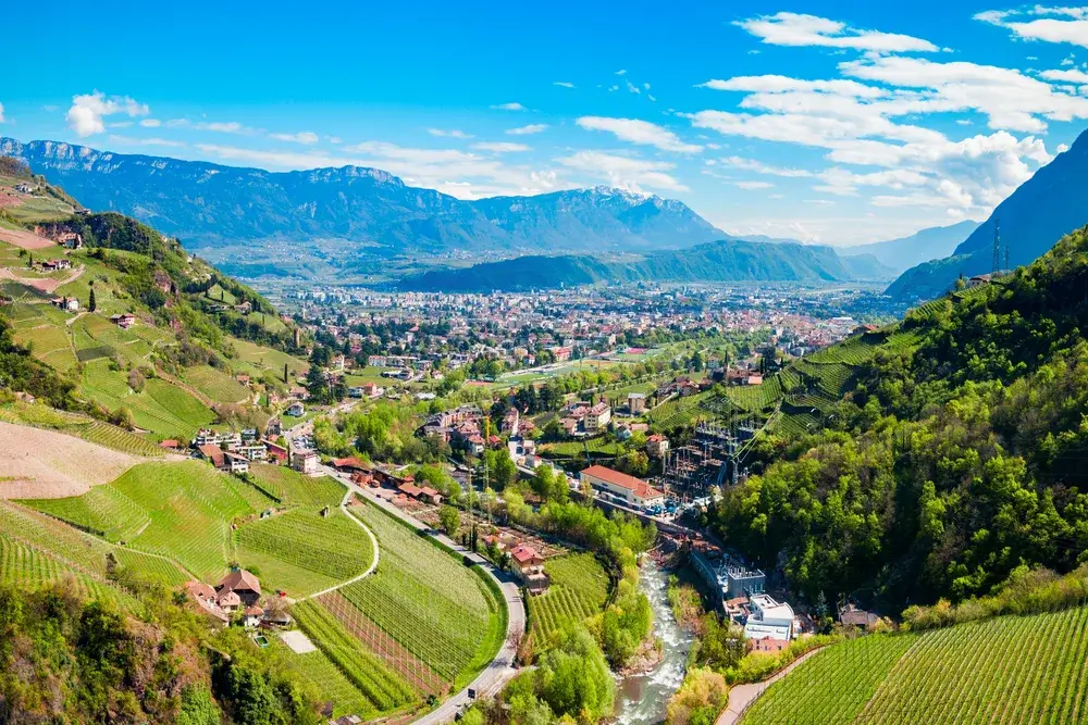 Luftfoto af Bolzano i dalen mellem vinmarker med Dolomitterne i baggrunden
