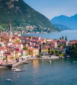 Den farverige landsby Varenna med kirketårn ved bredden af Comosøen og bjergene bag