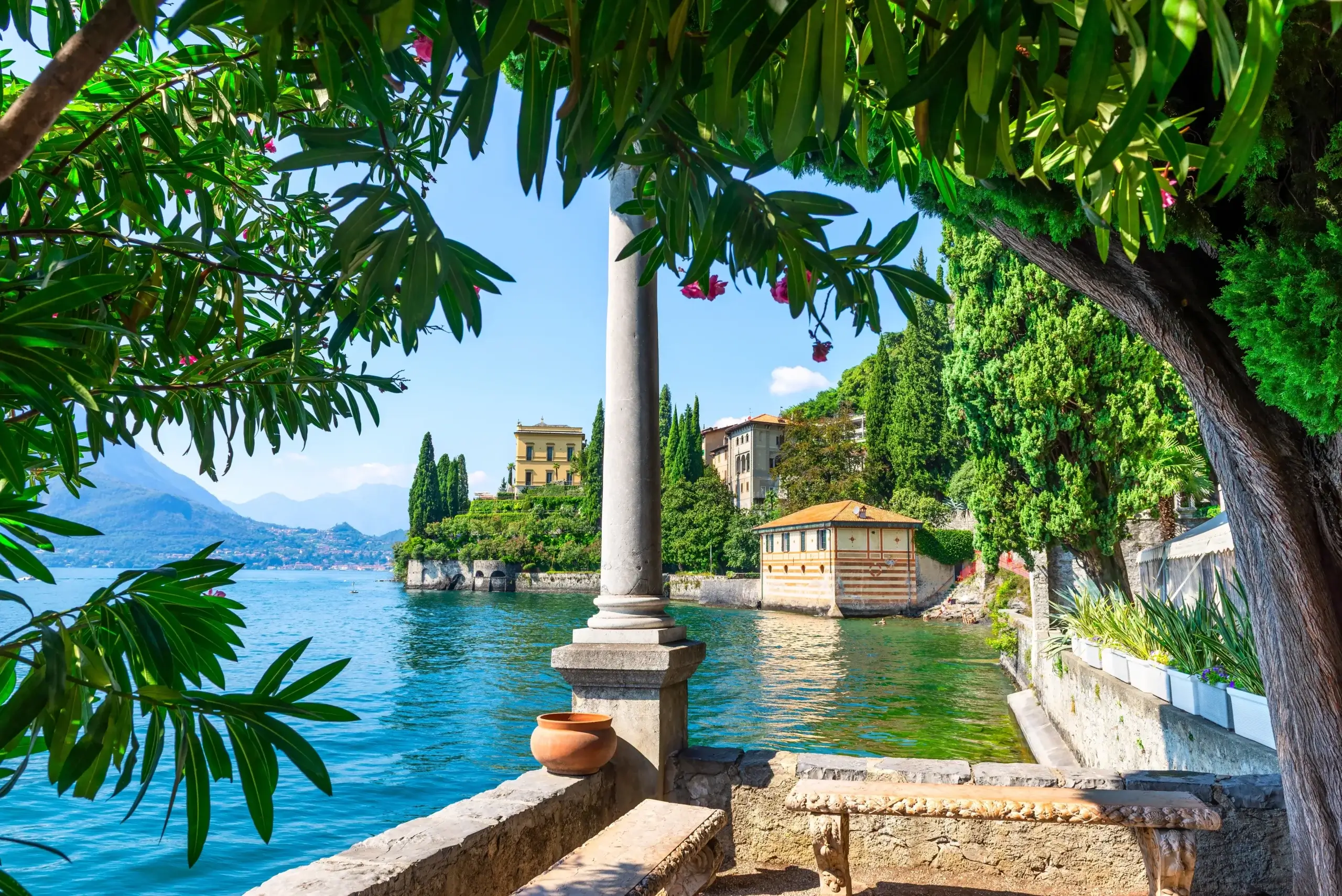 Udsigt fra haven ved Villa Monastero i Varenna mellem søjler og træer ud over Comosøen