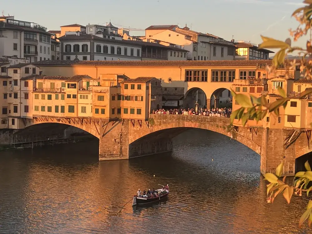 Ponte Vecchio over Arno-floden i Firenze i gyldent aftenlys med en robåd på vandet