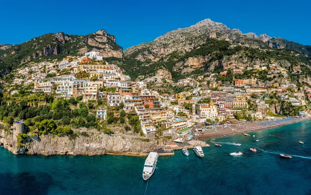 Positano med farvede huse ned ad klippen og stranden ved det blå hav på Amalfikysten