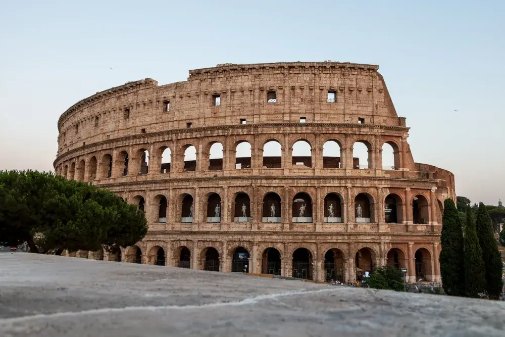 Colosseums buegange i lys sten set fra en terrasse med pinjetræer i Rom