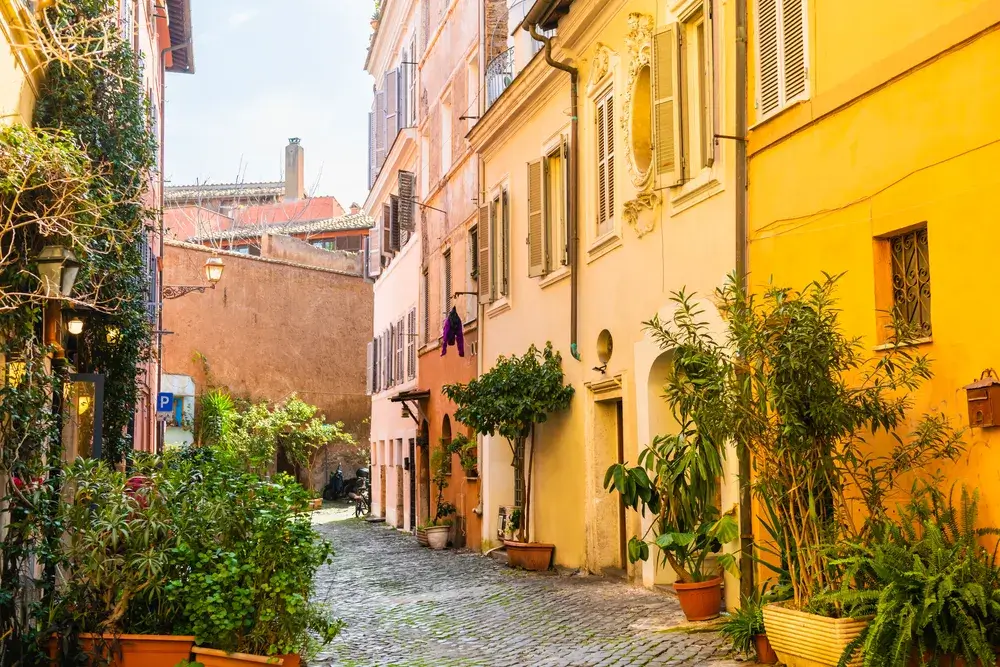 Smal gade med gule og orange huse og grønne planter i Trastevere i Rom