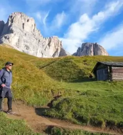 Vandrer med rygsæk på en sti over grønne enge under Langkofel-massivet i Dolomitterne