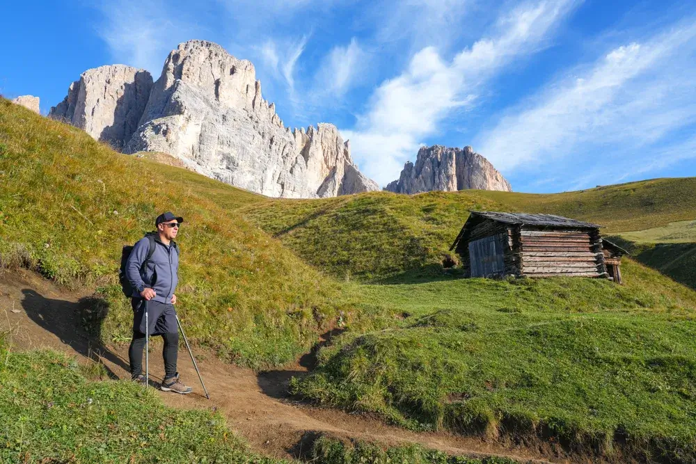 Vandrer med rygsæk på en sti over grønne enge under Langkofel-massivet i Dolomitterne