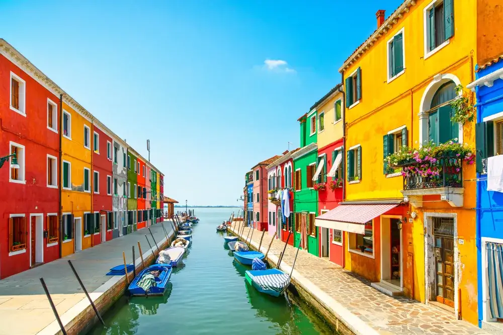 Farvestrålende huse langs en kanal med små både på øen Burano i Venedigs lagune