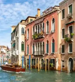 Farvestrålende middelalderpalæer med spidsbuede vinduer langs Canal Grande i Venedig og en træbåd på vandet