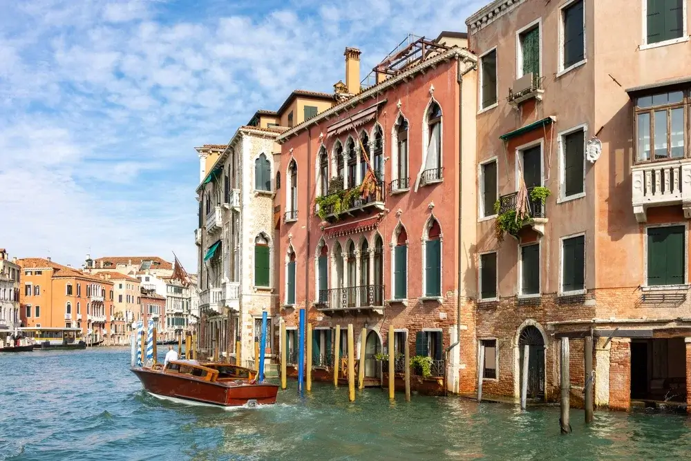 Farvestrålende middelalderpalæer med spidsbuede vinduer langs Canal Grande i Venedig og en træbåd på vandet