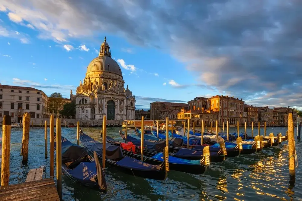 Fortøjede gondoler ved træpæle på Canal Grande med Santa Maria della Salute i morgenlys i Venedig