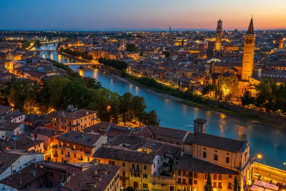 Luftfoto af Verona i skumringen med Adige-floden, broer og oplyste kirketårne i den gamle bydel