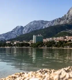 Stenstranden i Makarska med klart vand og bjerget Biokovo bag byen