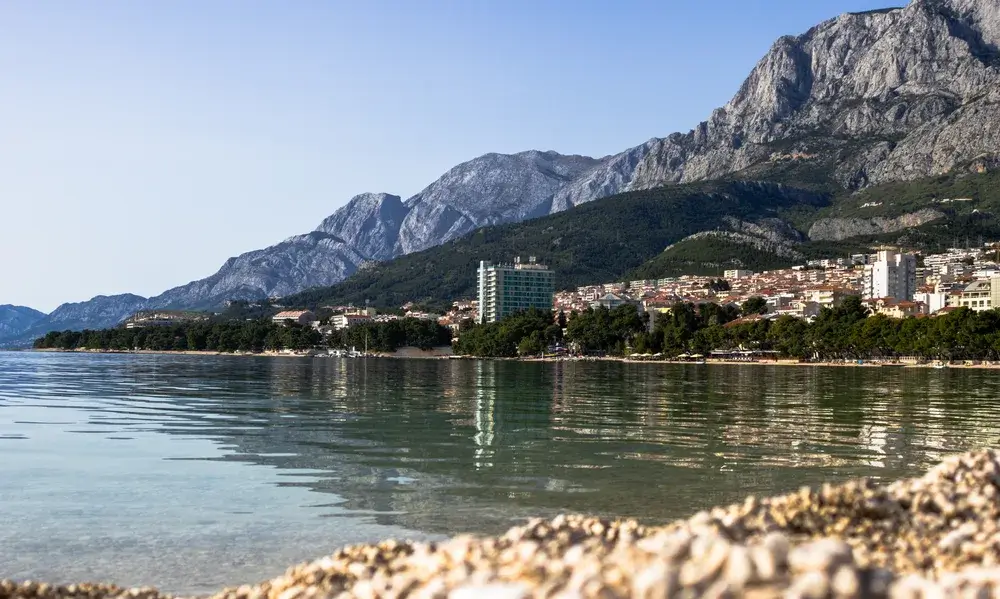 Stenstranden i Makarska med klart vand og bjerget Biokovo bag byen