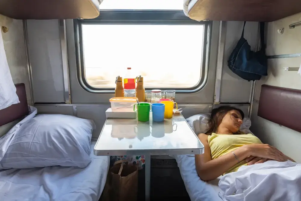 Kvinde sover i en togkupé med lille bord ved vinduet og senge på begge sider