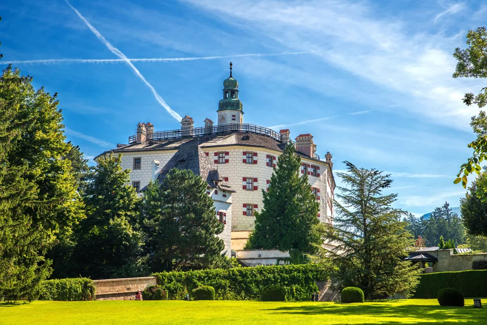 Schloss Ambras over Innsbruck med tårn og grønne haver under blå himmel