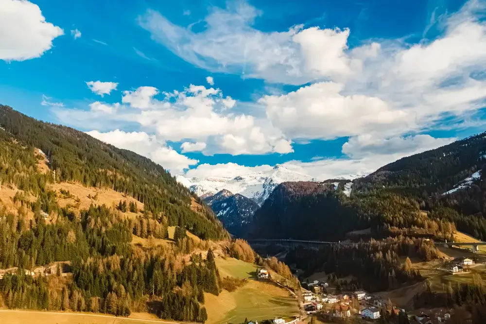 Grøn alpedal ved Brennerpasset mellem Østrig og Italien med skovklædte bjerge og sne på toppene