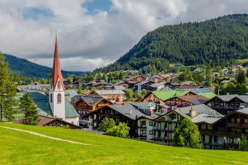 Seefeld in Tirol med kirketårn, træhuse og skovklædte bjerge set fra engen