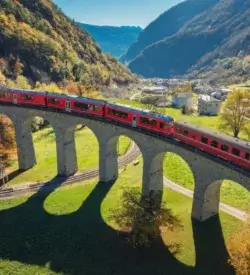 Det røde Bernina Express-tog kører over den runde Brusio-viadukt i en grøn alpedal