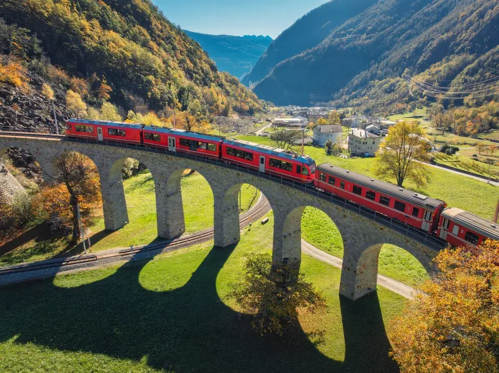 Det røde Bernina Express-tog kører over den runde Brusio-viadukt i en grøn alpedal