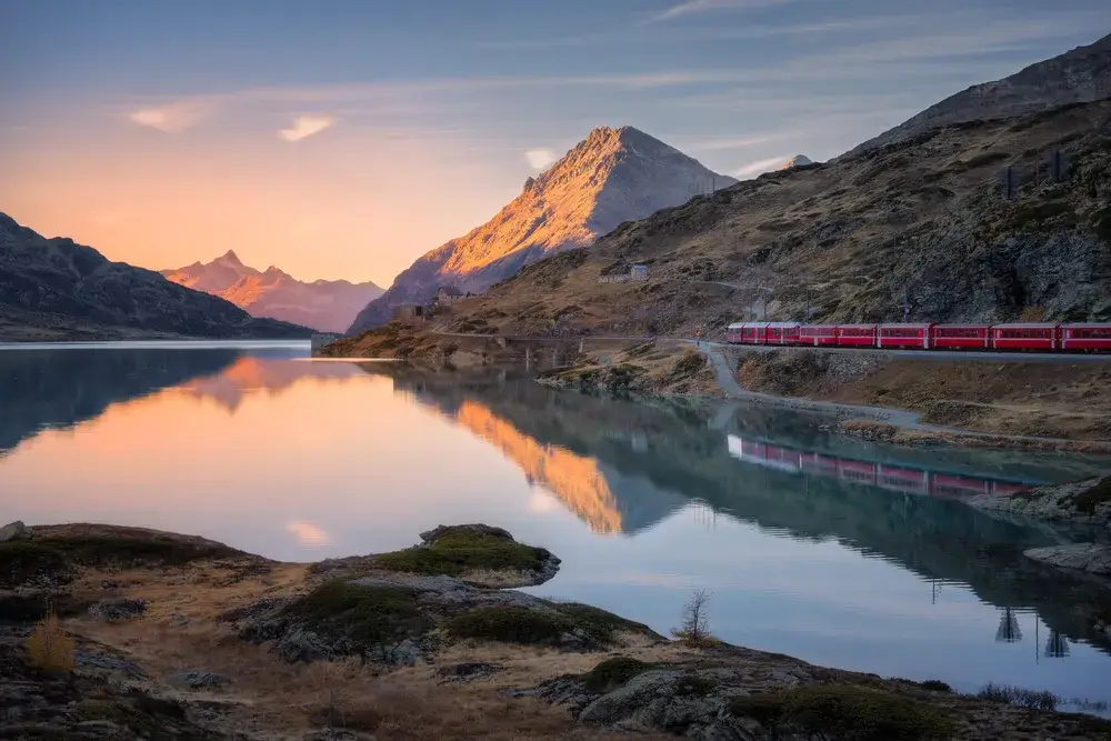 Det røde Bernina Express-tog langs Lago Bianco ved Berninapasset i aftenlys
