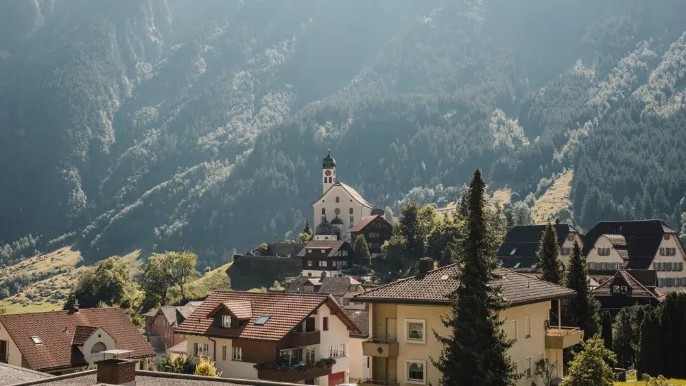 Landsbyen Wassen med den hvide kirke på skrænten i Reussdalen under de skovklædte alper