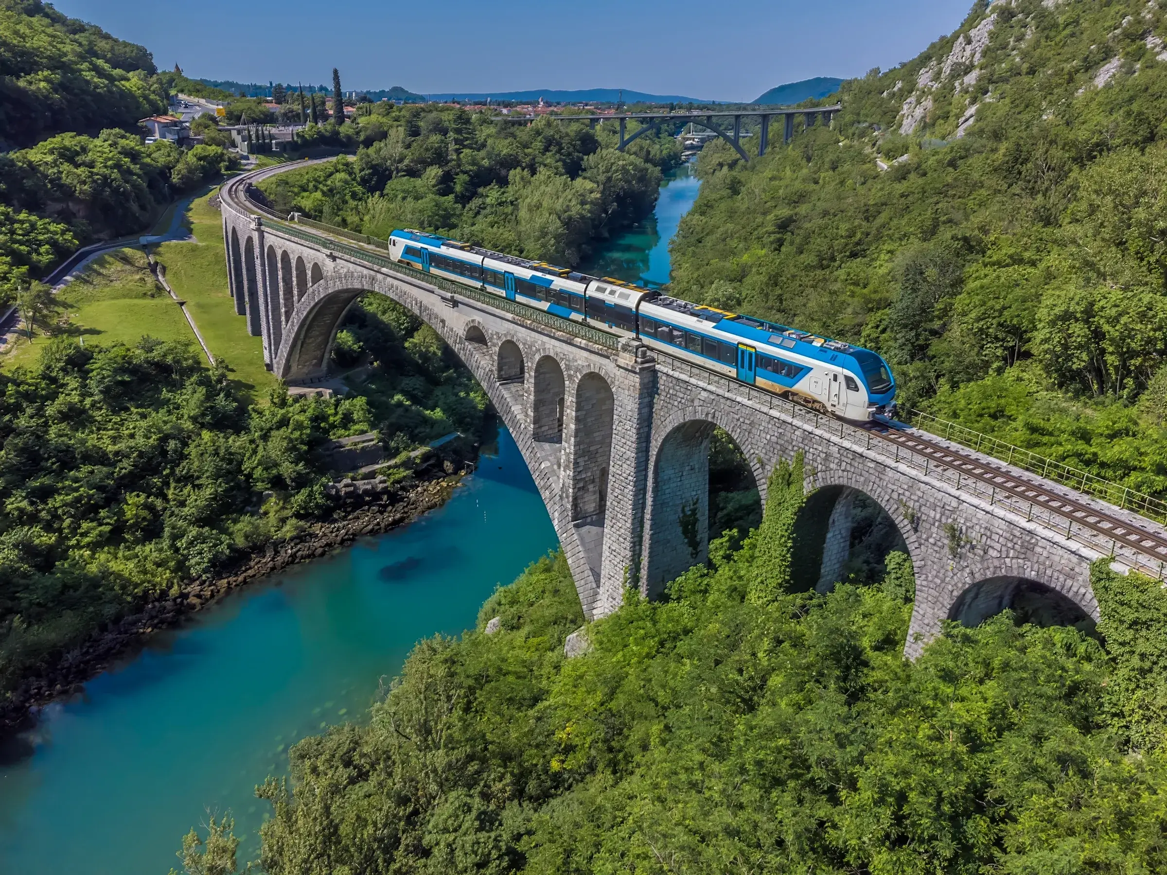 Blåt og hvidt passagertog på stenbroen ved Solkan over den turkise flod Soča