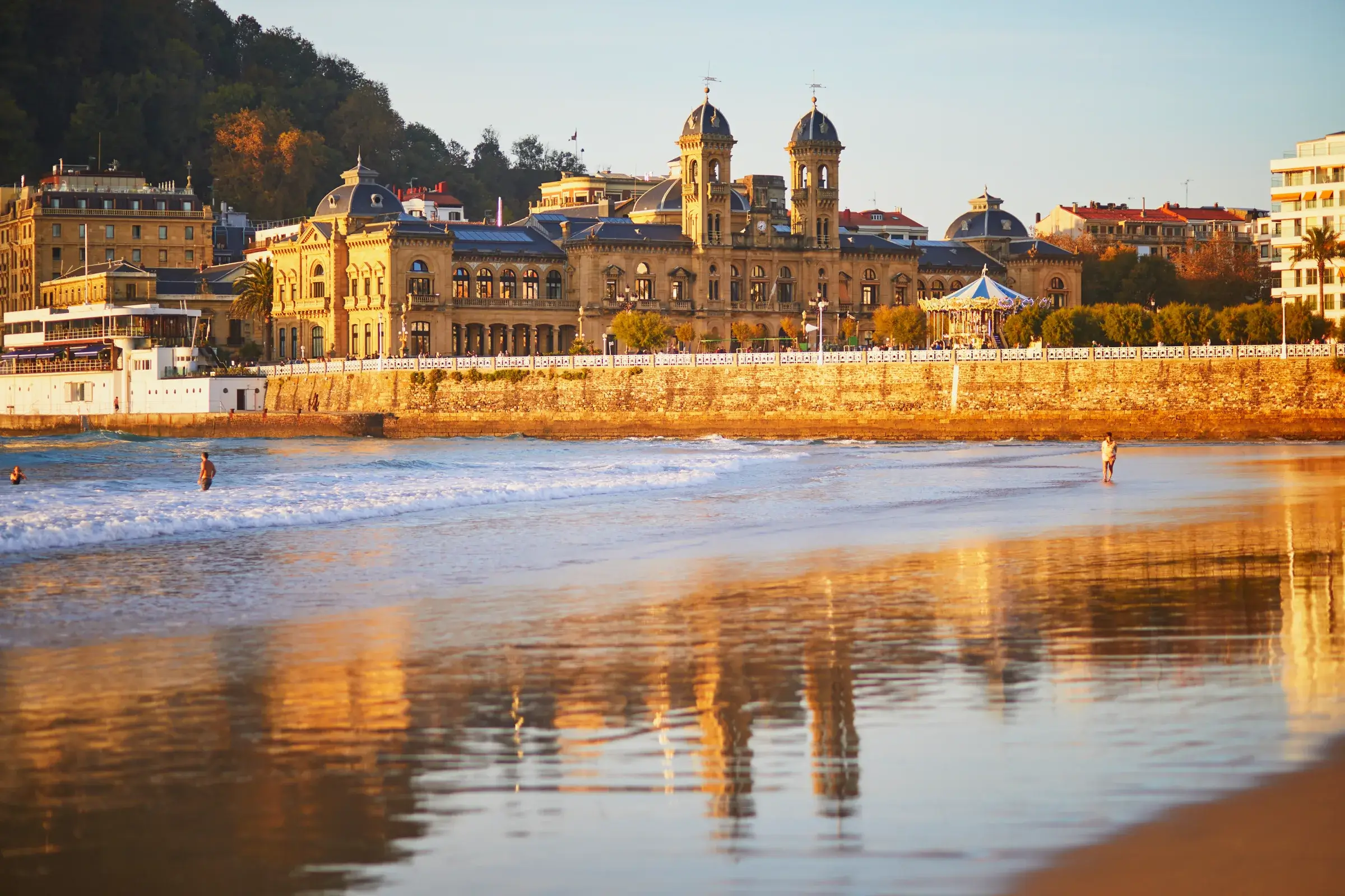 La Concha-stranden i aftenlys med rådhuset i San Sebastián spejlet i vådt sand
