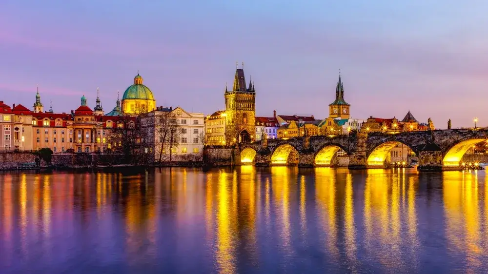 Den oplyste Karlsbro og brotårnene spejler sig i Vltava-floden i Prag i aftenlys