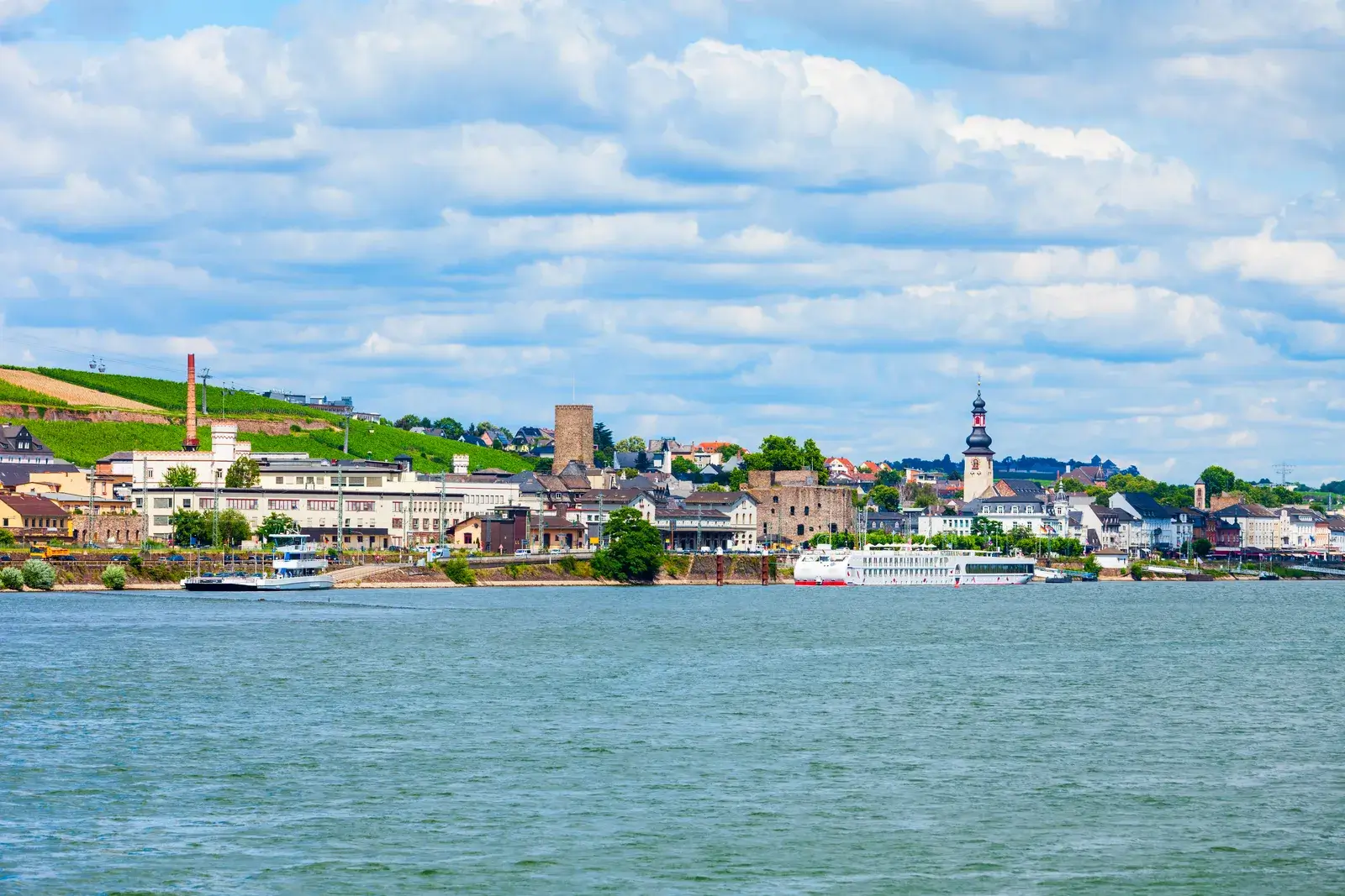 Rüdesheim am Rhein med vinbjerge, kirketårn og en flodbåd set fra Rhinen